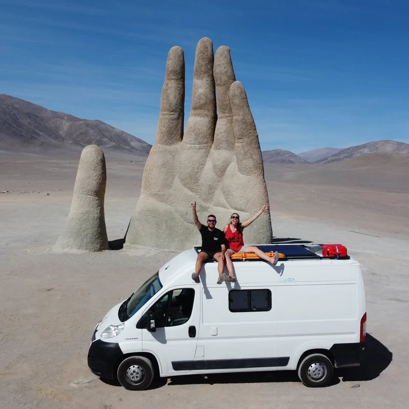 Pareja overland en su van camper, con paneles solares, junto a la Mano del Desierto en el desierto de Atacama, Chile