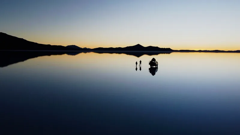 Pareja y 4x4 overland con tienda de techo en el Salar de Uyuni, Bolivia, al amanecer, reflejados en el agua