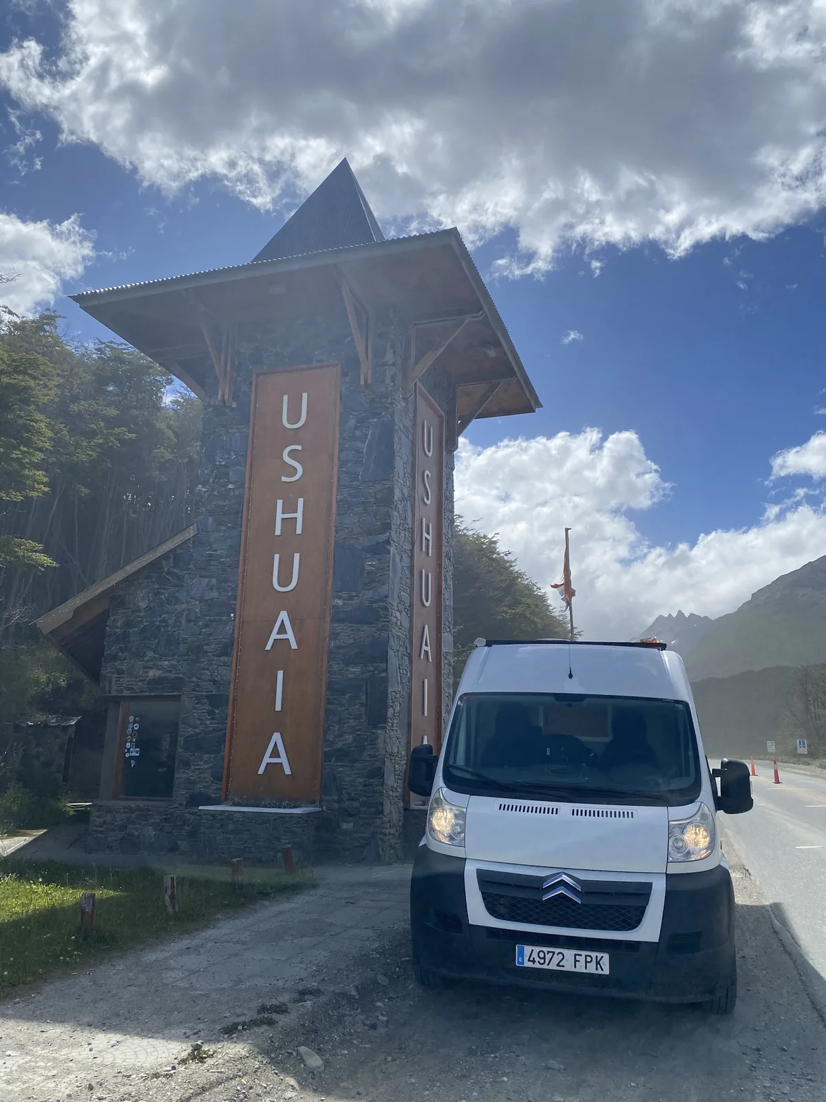 Overland van blanca ante el icónico cartel de piedra de Ushuaia, Fin del Mundo, Argentina, bajo un cielo patagónico