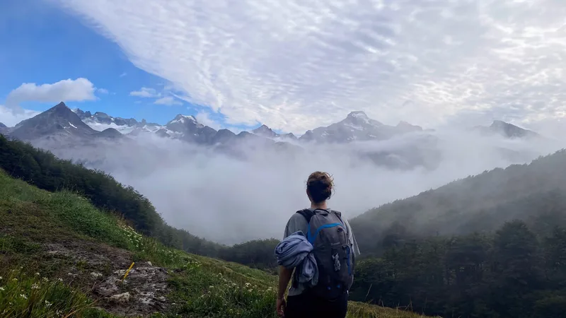 Senderista con mochila observando imponentes montañas nevadas entre la niebla en una ruta de trekking patagónico