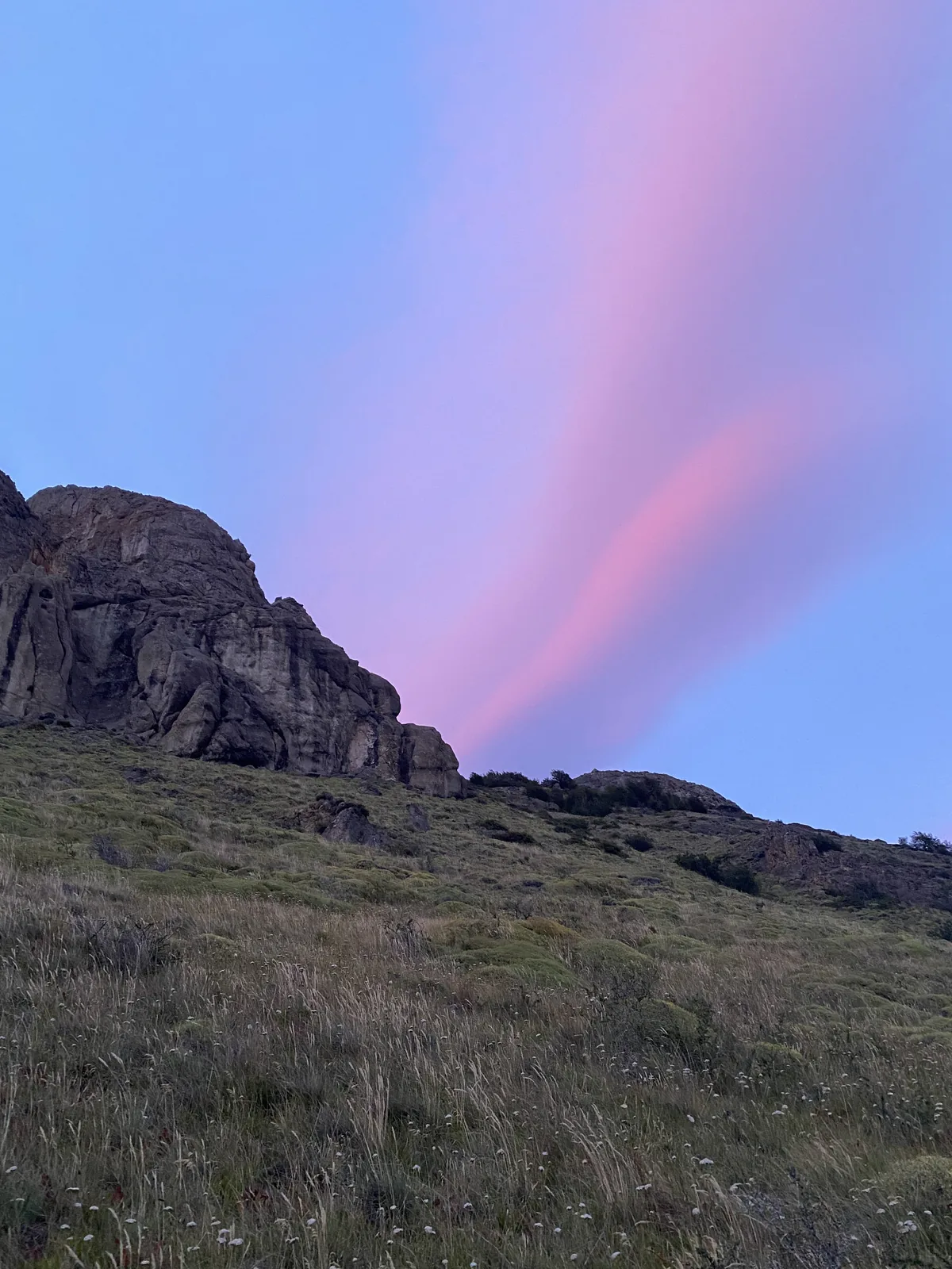 Atardecer espectacular con rayos rosados y morados cruzando el cielo sobre una montaña árida y pastizales, espíritu overland