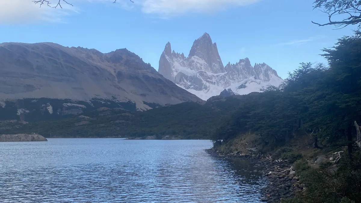Paisaje patagónico con el imponente Monte Fitz Roy y sus picos nevados, un lago sereno y bosque denso