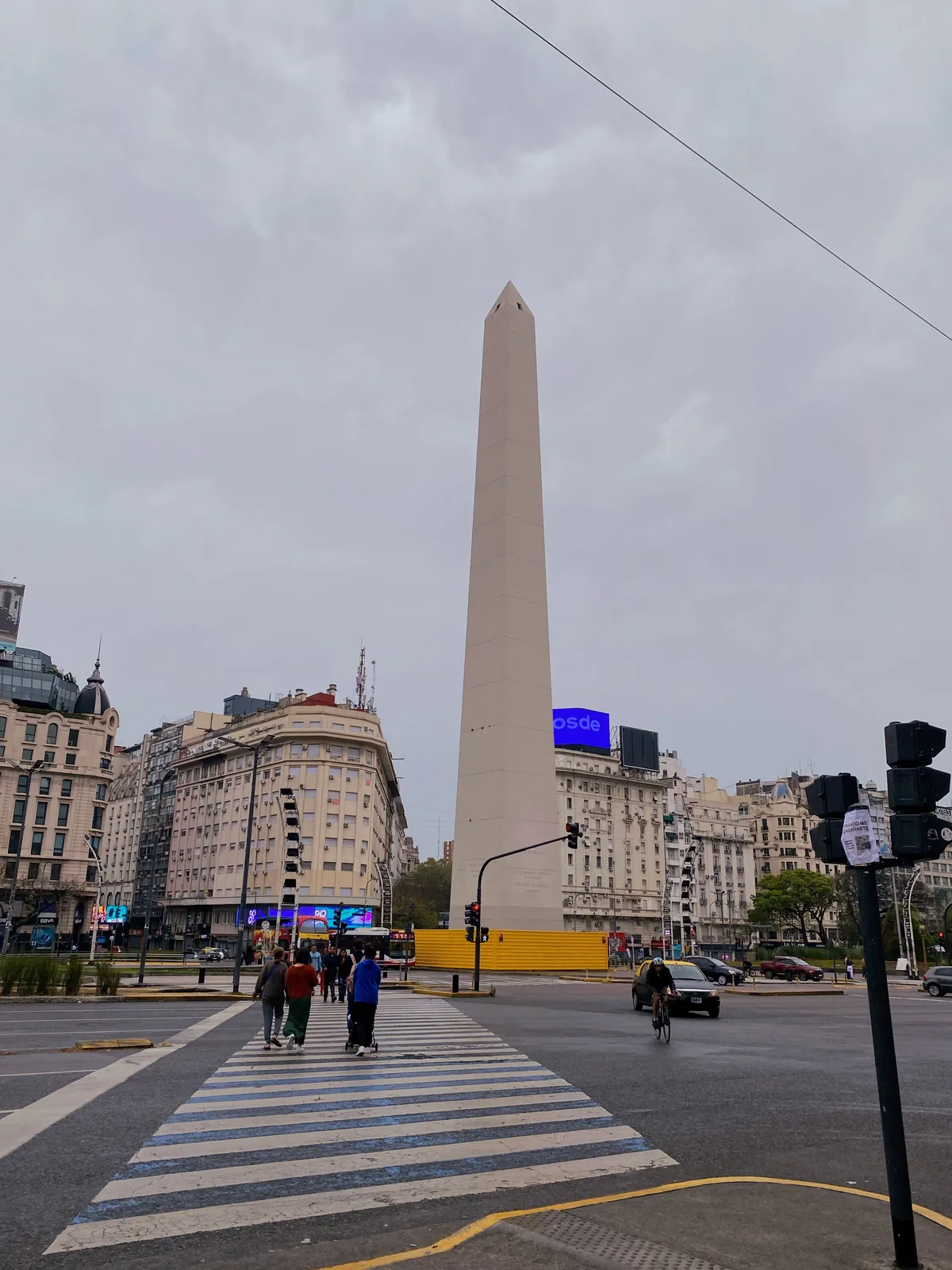 Obelisco de Buenos Aires en la Plaza de la República con peatones y tráfico urbano bajo un cielo gris.