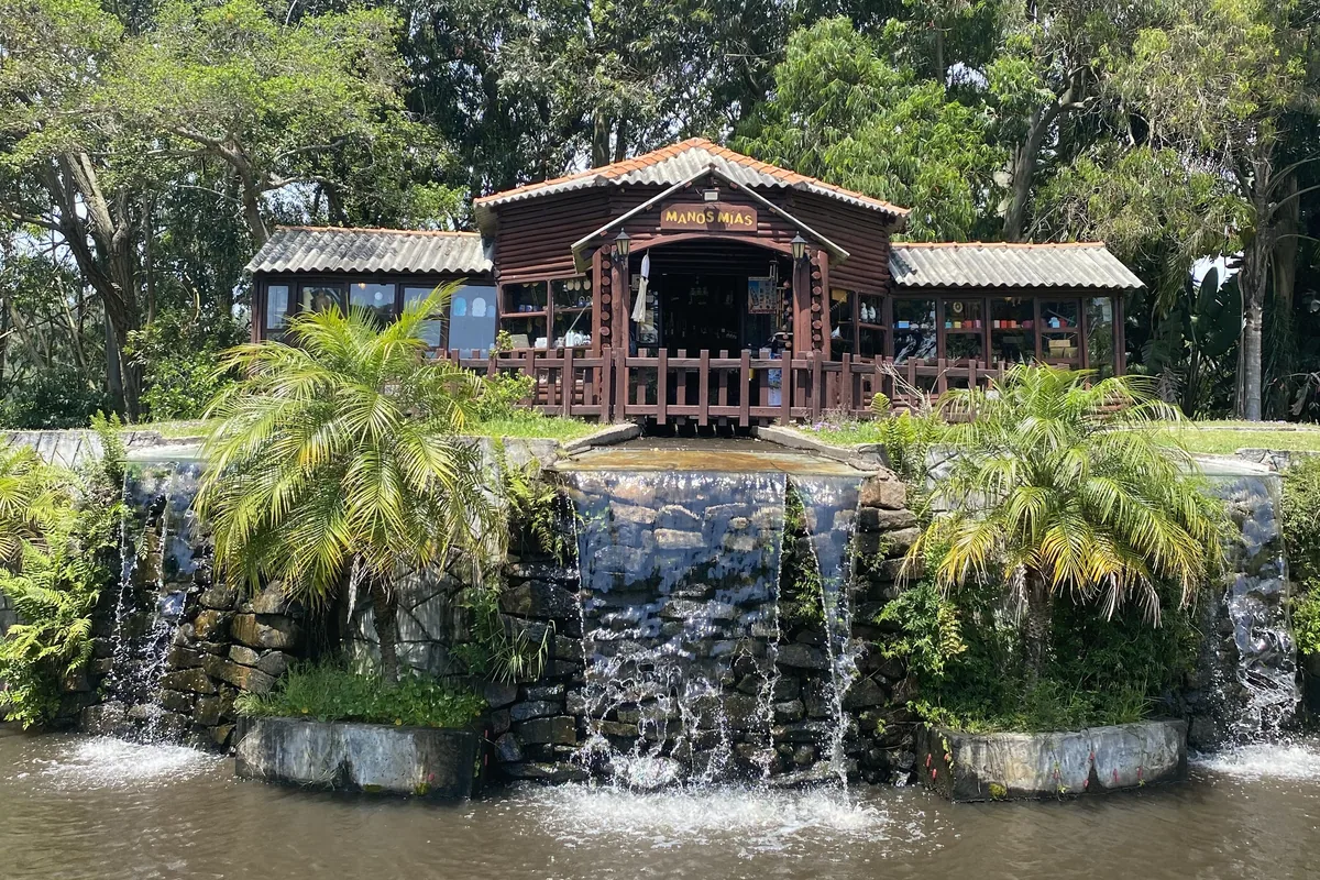 Edificio rústico "Manos Mías" con cascada artificial de rocas, rodeado de palmeras y abundante vegetación tropical