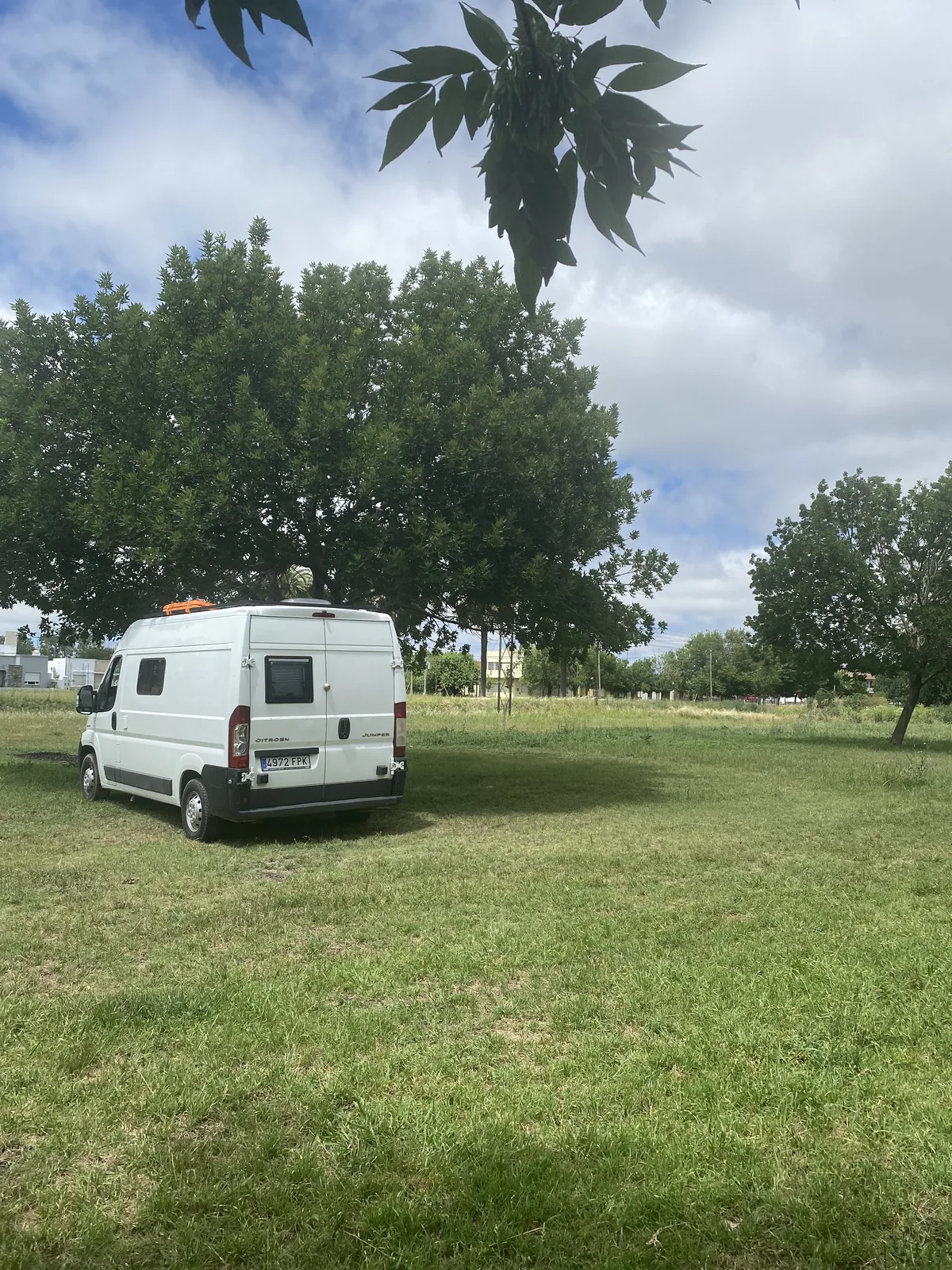 Furgoneta camper Citroën Jumper blanca con panel solar y antena satelital, estacionada en un campo verde arbolado