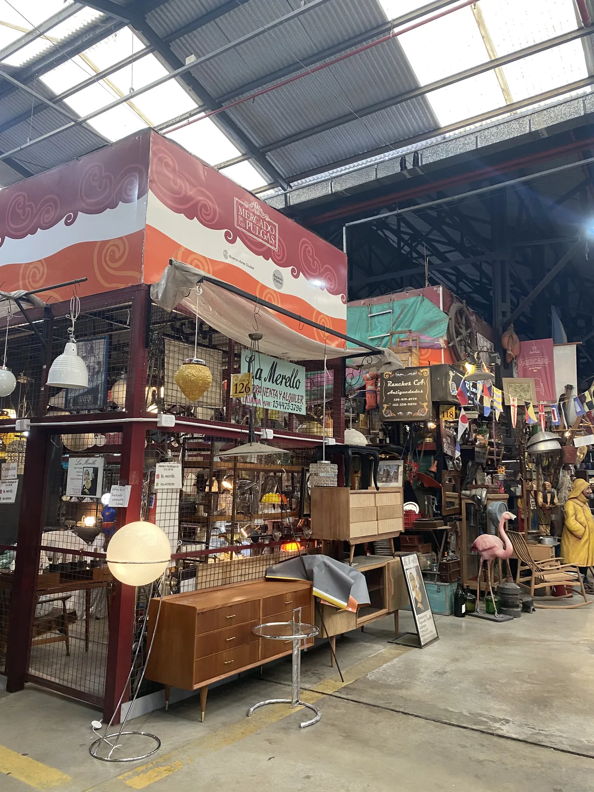 Interior de un Mercado de Pulgas con puestos de antigüedades, lámparas y mobiliario vintage. Techo industrial con luz natural