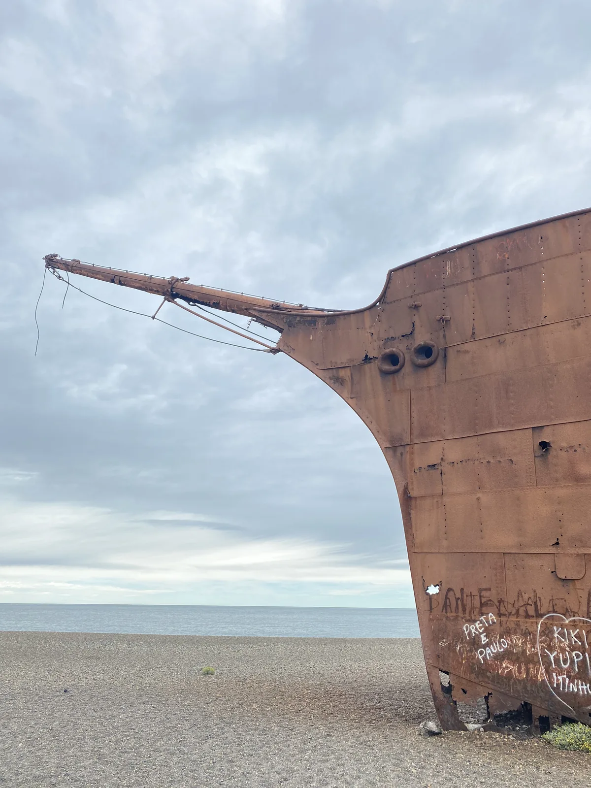 Proa de buque oxidado encallado en una solitaria playa de guijarros frente al mar. Paisaje ideal para una aventura overland