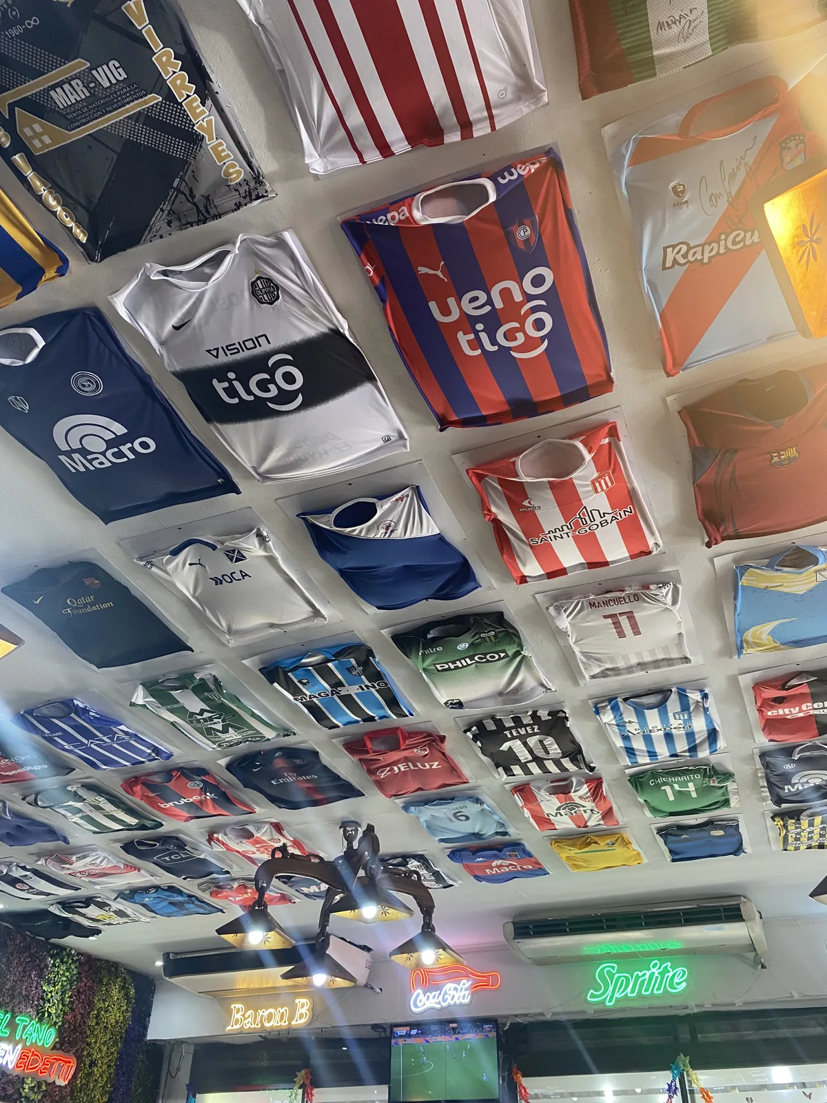 Techo de bar deportivo cubierto de decenas de camisetas de fútbol enmarcadas de clubes de Paraguay y Argentina