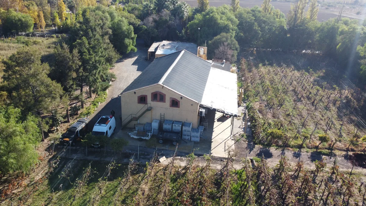Vista aérea de una bodega de viñedos con una van camper con paneles solares y un 4x4 estacionados, rodeada de campo