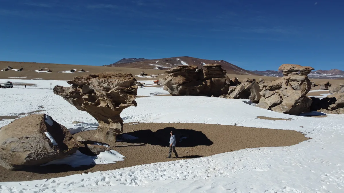 Formación rocosa Árbol de Piedra en el desierto de Siloli, Bolivia, con nieve y montañas. Un viajero explora la zona