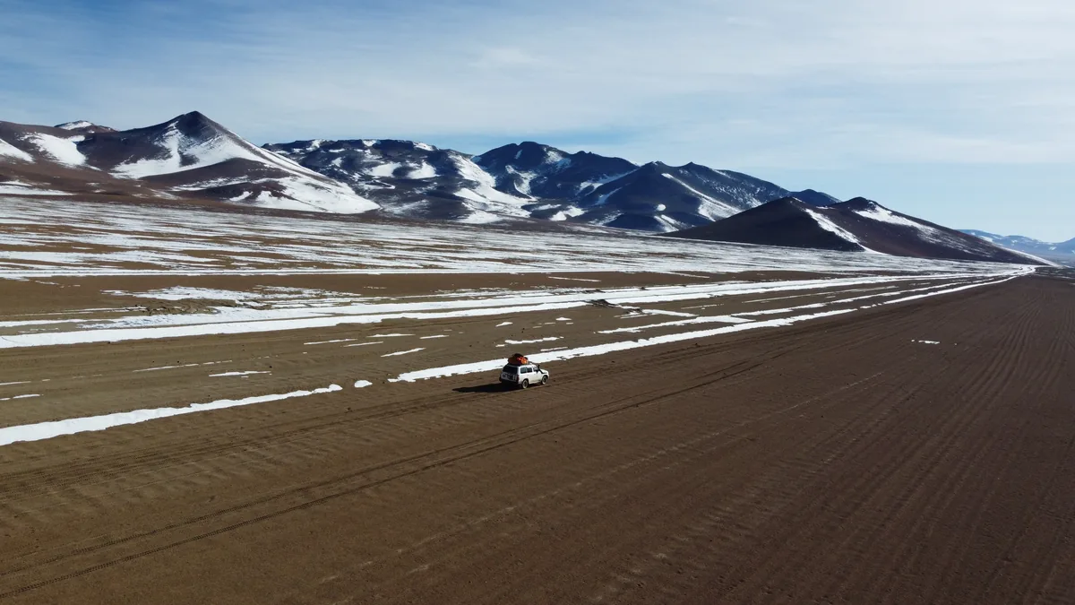 Rodando en un 4x4 por una remota pista de tierra con nieve en el altiplano andino y montañas nevadas al fondo