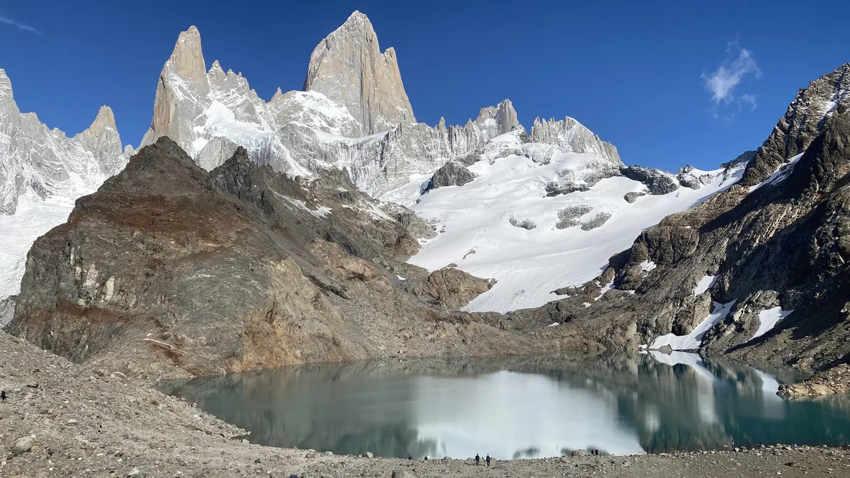 Senderistas frente al Fitz Roy y la Laguna de los Tres, cumbres nevadas y glaciar, reflejándose en el agua turquesa
