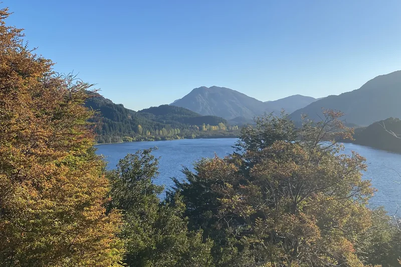 Luminoso lago de montaña con orillas cubiertas de densos bosques y árboles con hojas otoñales en la Patagonia