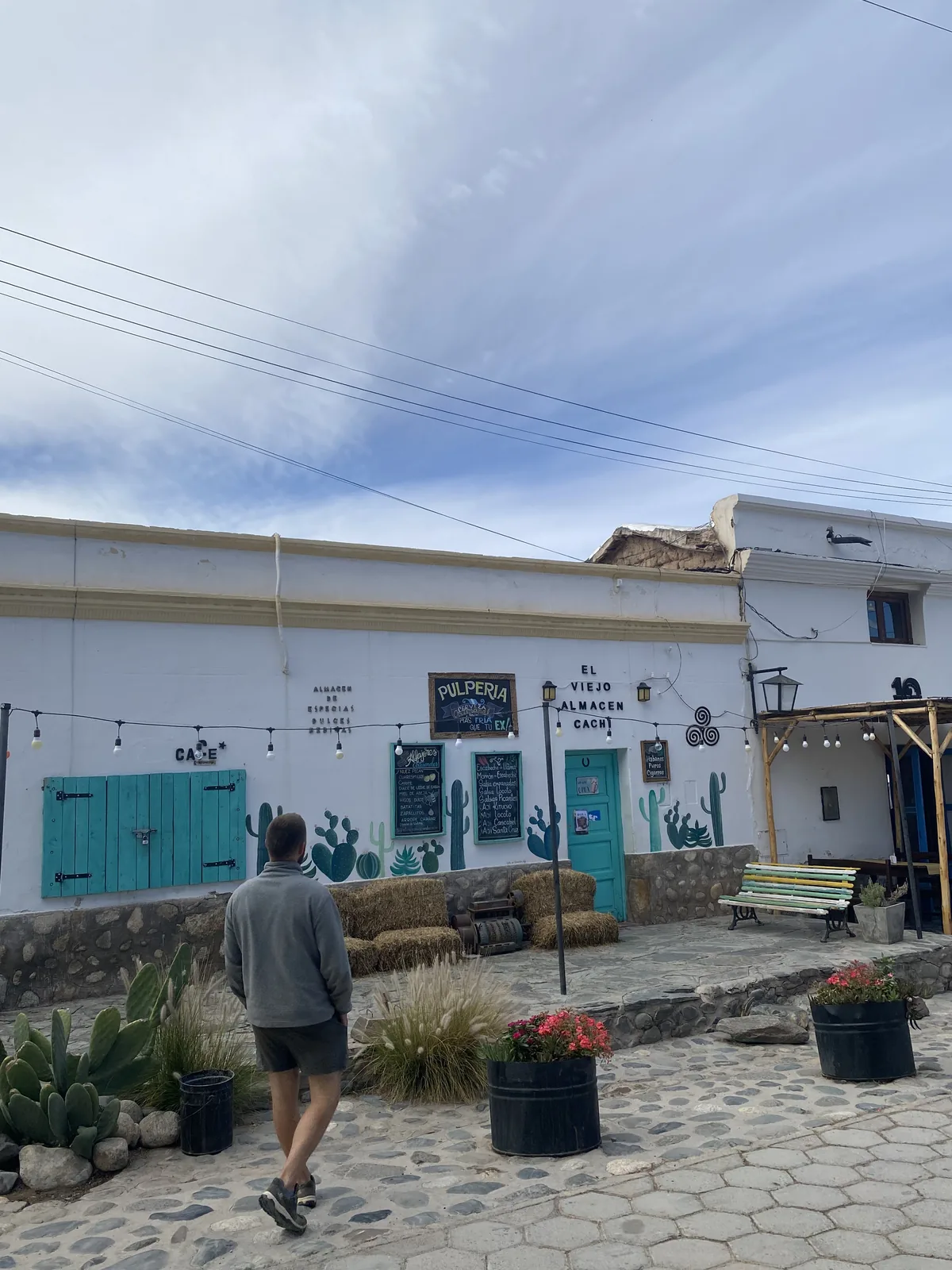 Hombre caminando por la calle empedrada hacia El Viejo Almacén Pulpería en Cachi, Salta, con decoración de cactus