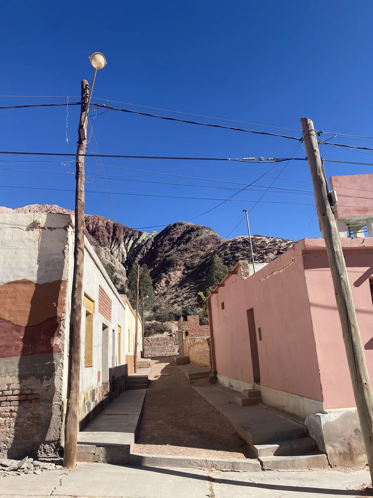 Callejón empinado en Purmamarca con casas de colores pastel, postes de madera y el Cerro de los Siete Colores al fondo