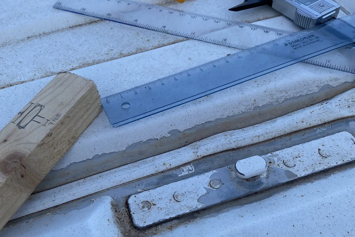 Reglas, calibre y madera marcada sobre el techo de una furgoneta, preparando modificaciones para un viaje overland