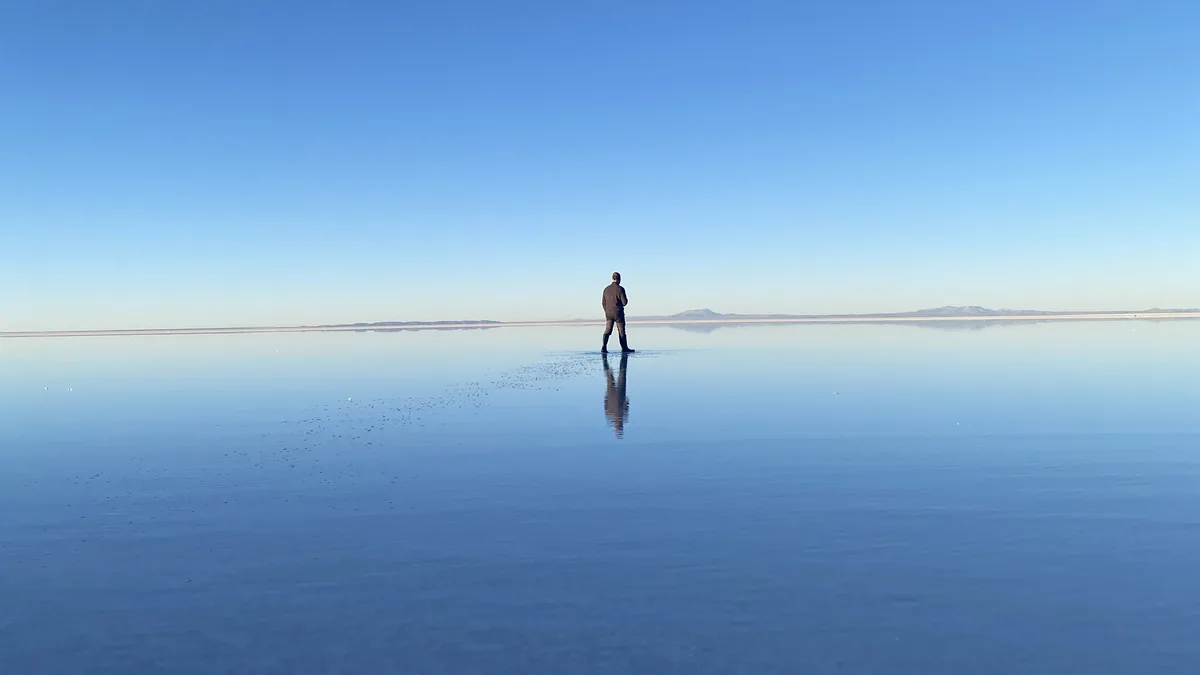 Viajero solitario en el Salar de Uyuni, donde el cielo azul se fusiona con la inmensa superficie de agua, creando un espejo