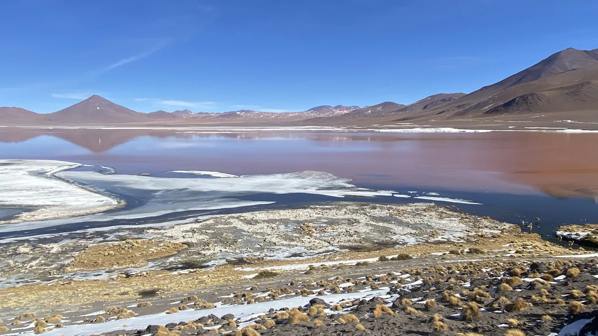 Rodando por el altiplano boliviano: Laguna Colorada con agua rojiza, hielo, flamencos y montañas áridas bajo cielo azul