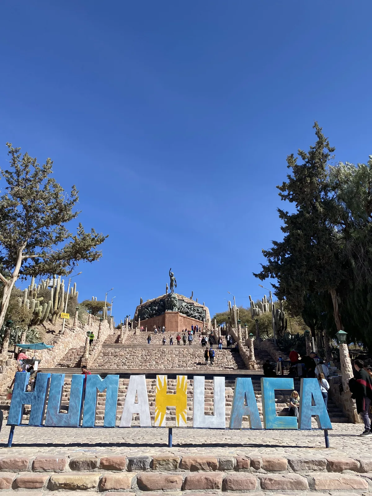 Cartel de Humahuaca, Jujuy, con el Monumento a los Héroes de la Independencia, escalinatas y cardones bajo sol andino