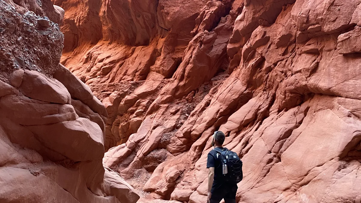 Viajero con mochila explorando un profundo cañón de arenisca roja con imponentes paredes esculpidas por la naturaleza