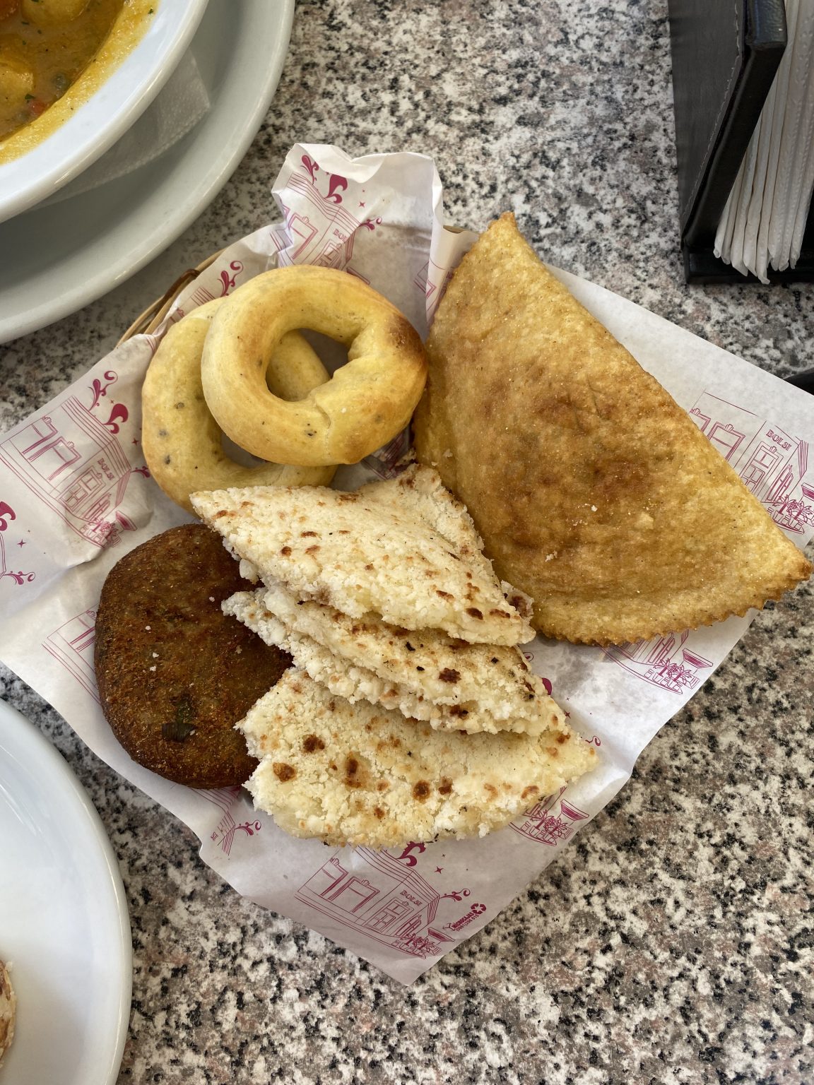 Cesta de fritos y panes variados con empanada, rosquillas, arepitas de yuca y croqueta sobre mesa de granito