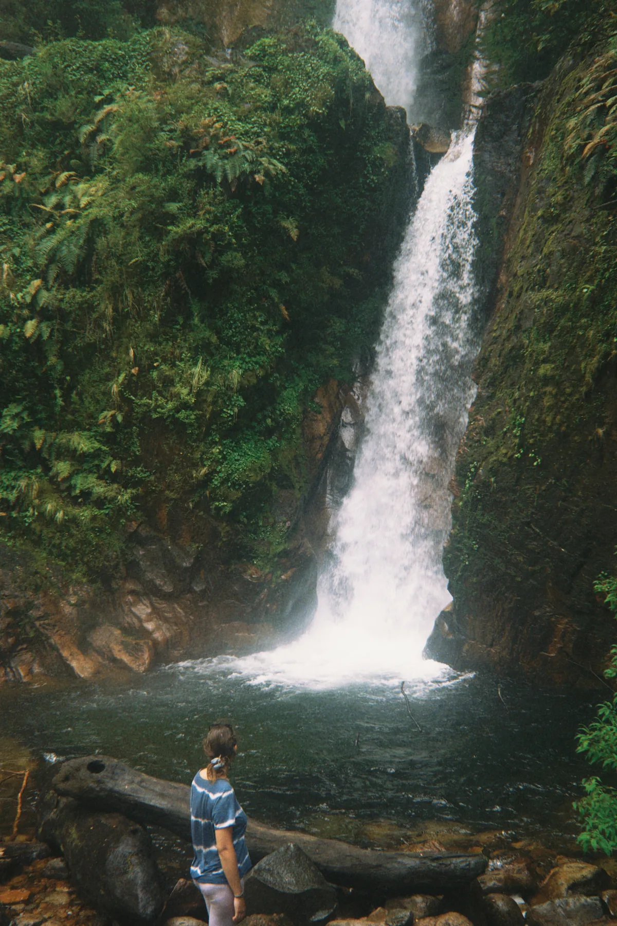 Viajera contemplando una gran cascada tropical rodeada de abundante vegetación y rocas en un hermoso paisaje natural