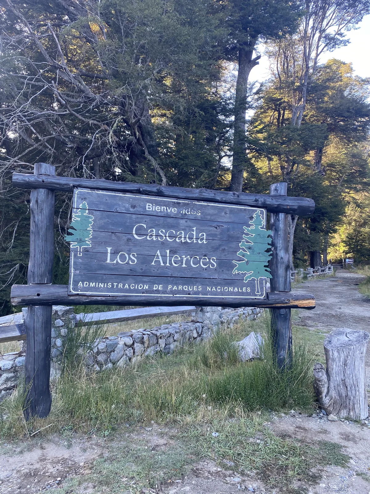 Cartel de bienvenida a la Cascada Los Alerces en el Parque Nacional, con un camino de tierra y frondoso bosque