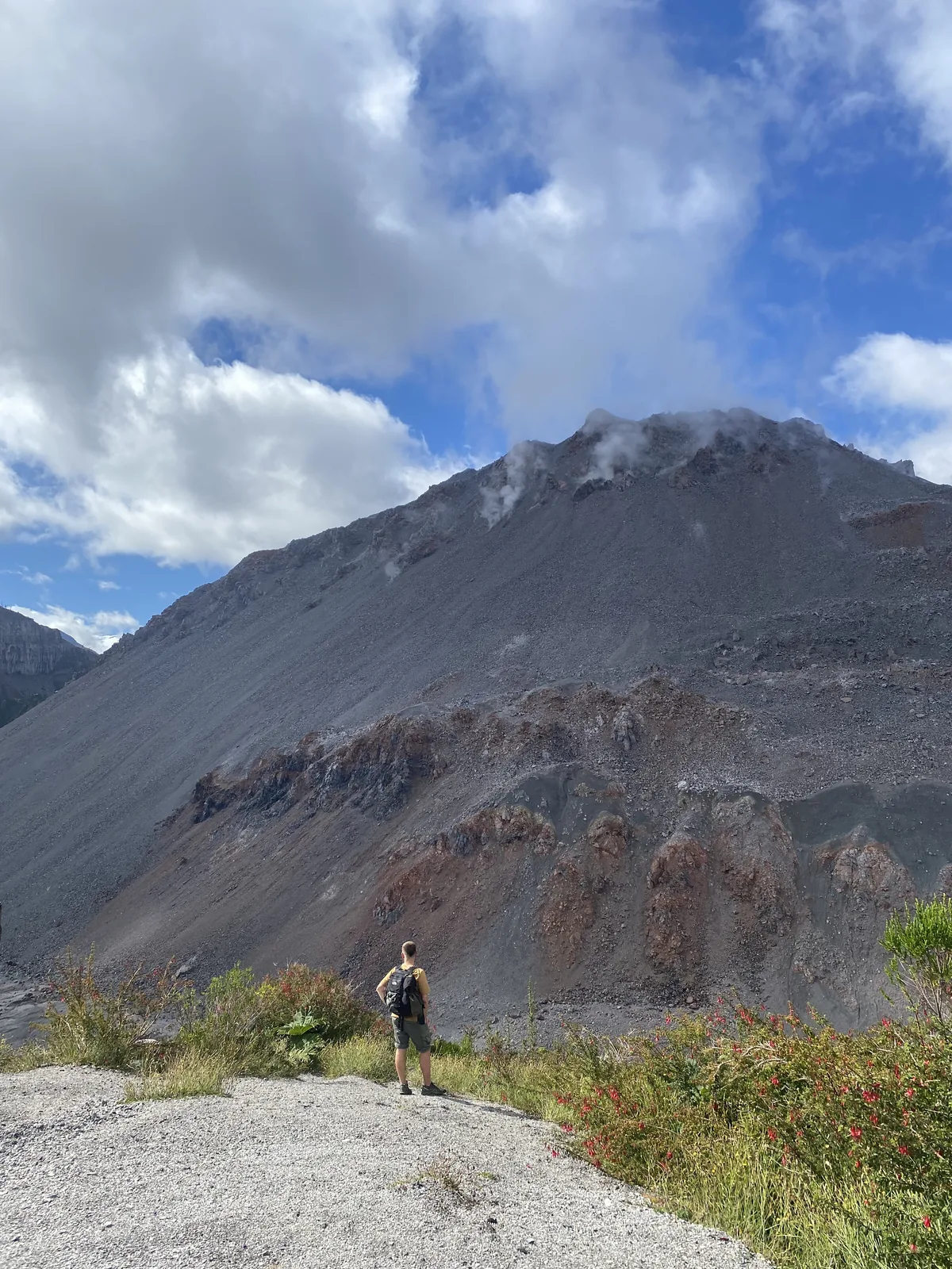 Viajero con mochila contemplando la cima de una montaña volcánica con vapor bajo un cielo azul nublado