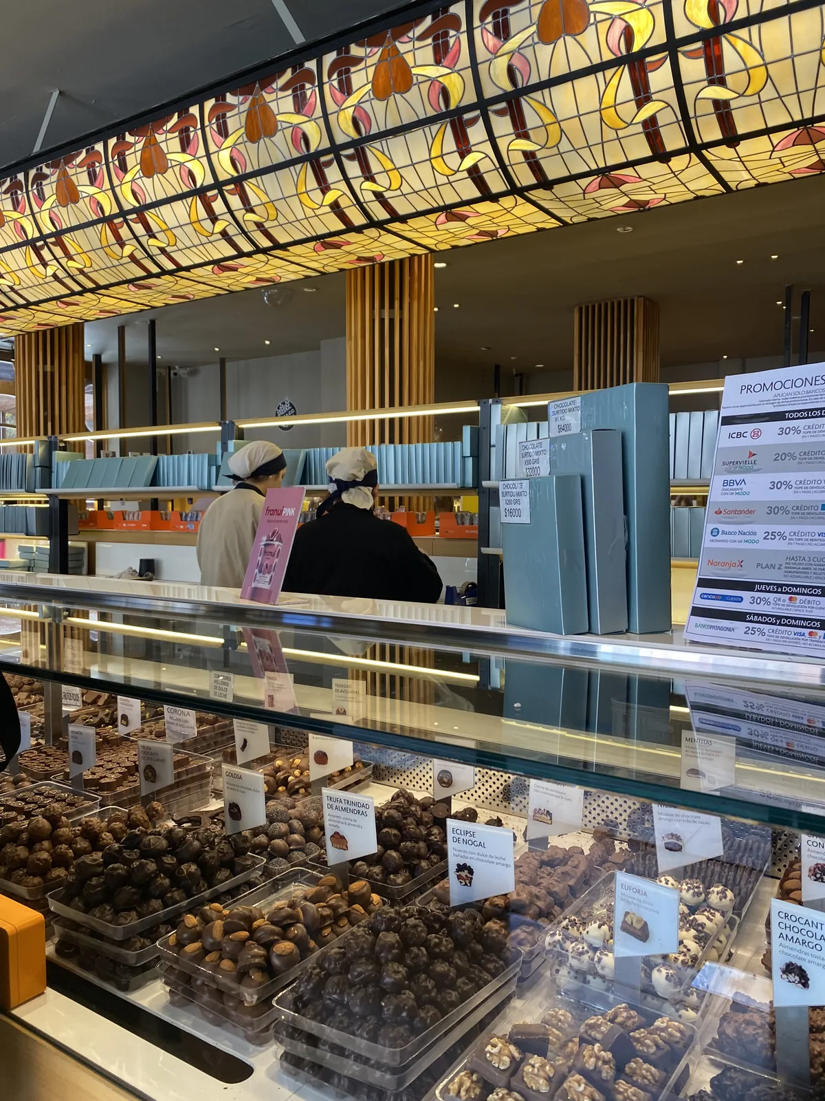 Tienda de chocolates con vitrinas de bombones, trufas de almendras y nuez, y empleados detrás del mostrador