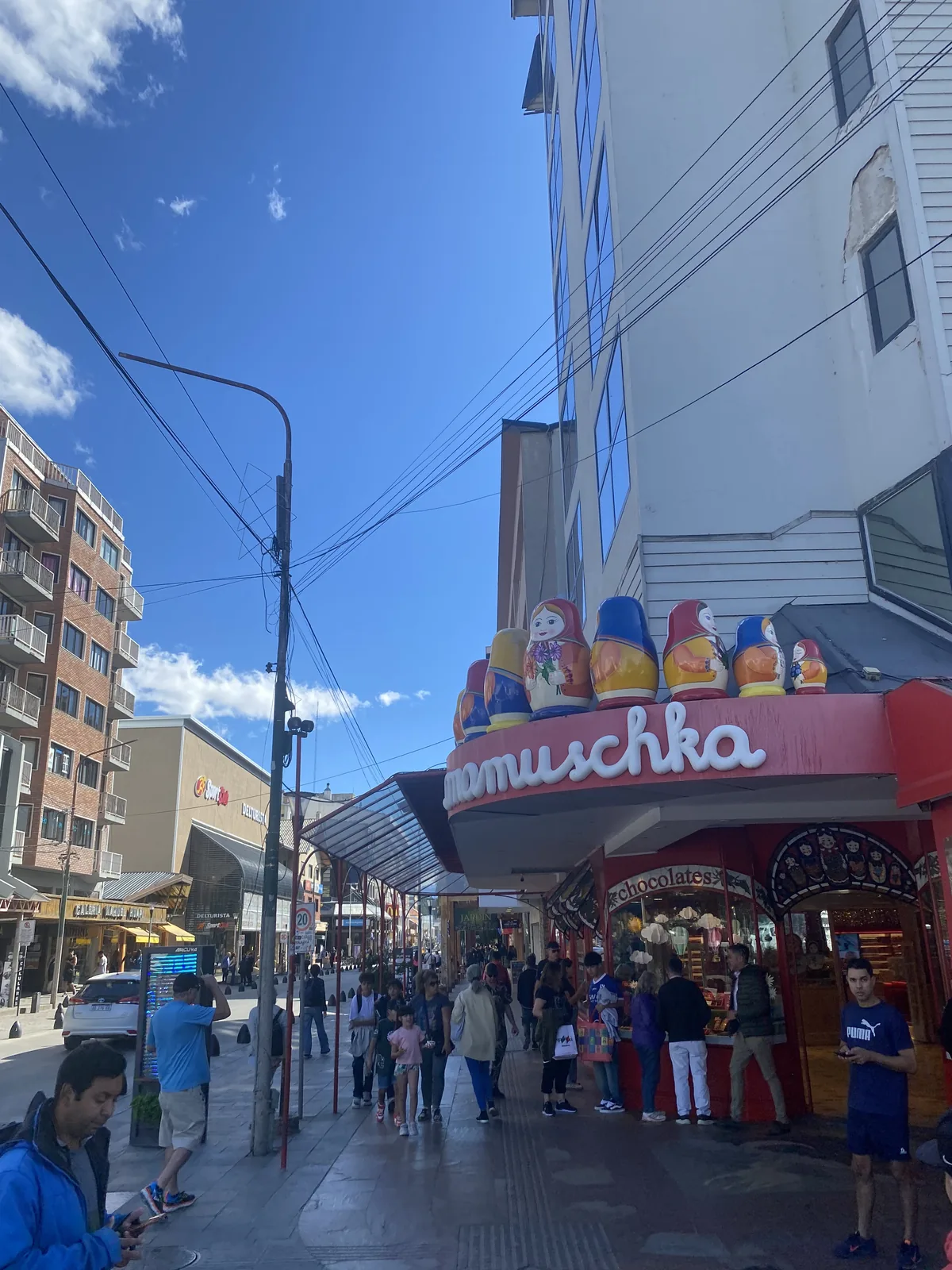Concurrida calle de Bariloche con la chocolatería Mamuschka, sus matryoshkas gigantes y gente paseando bajo cielo azul
