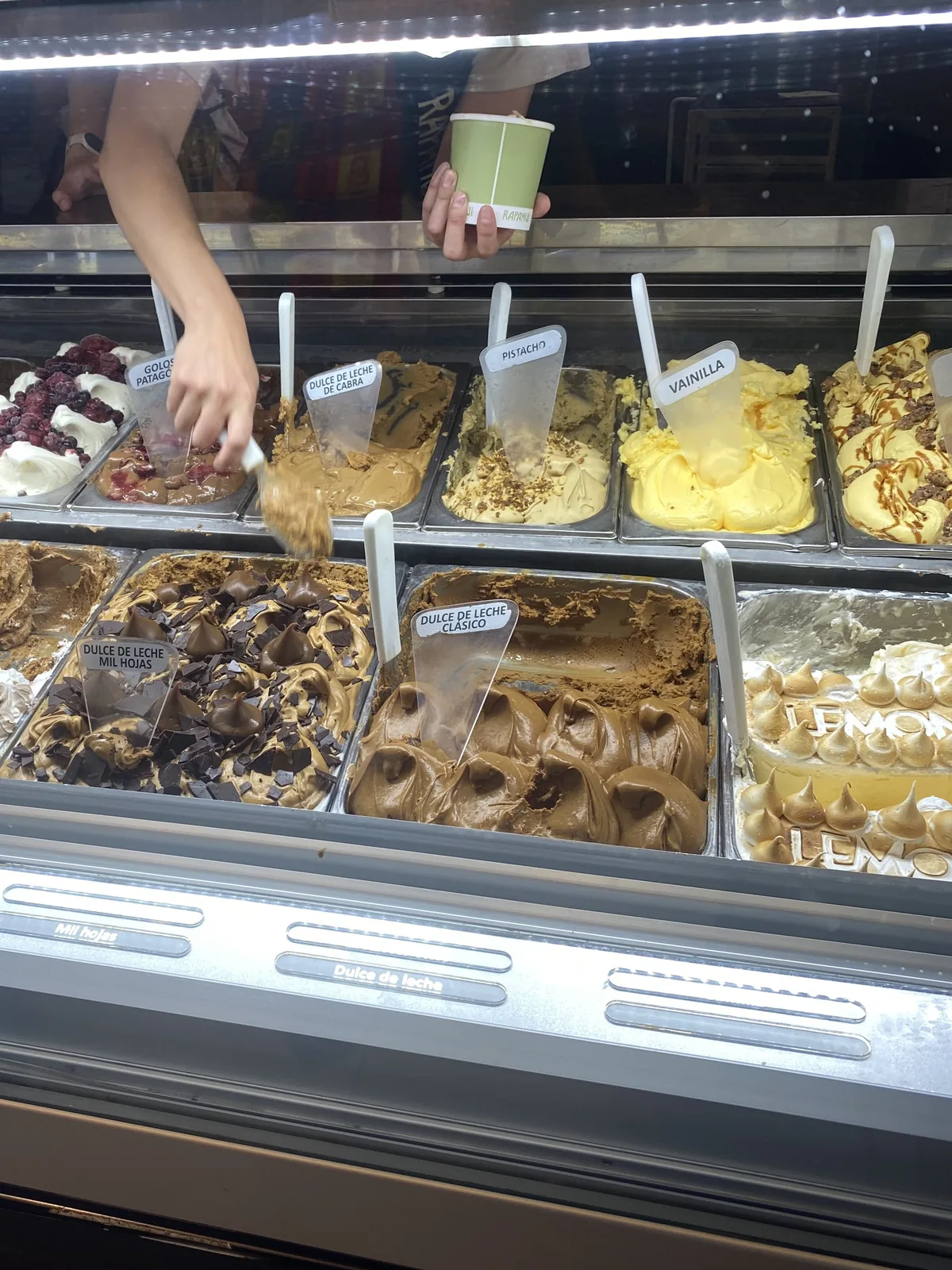 Manos sirviendo helado de dulce de leche de cabra y otros sabores Rapanui, un dulce stop en la ruta patagónica