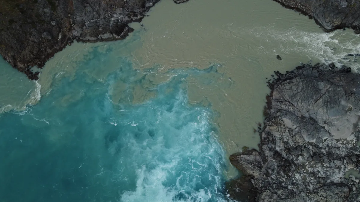 Confluencia de río glacial turquesa y río de aguas marrones entre orillas rocosas, creando un contraste natural