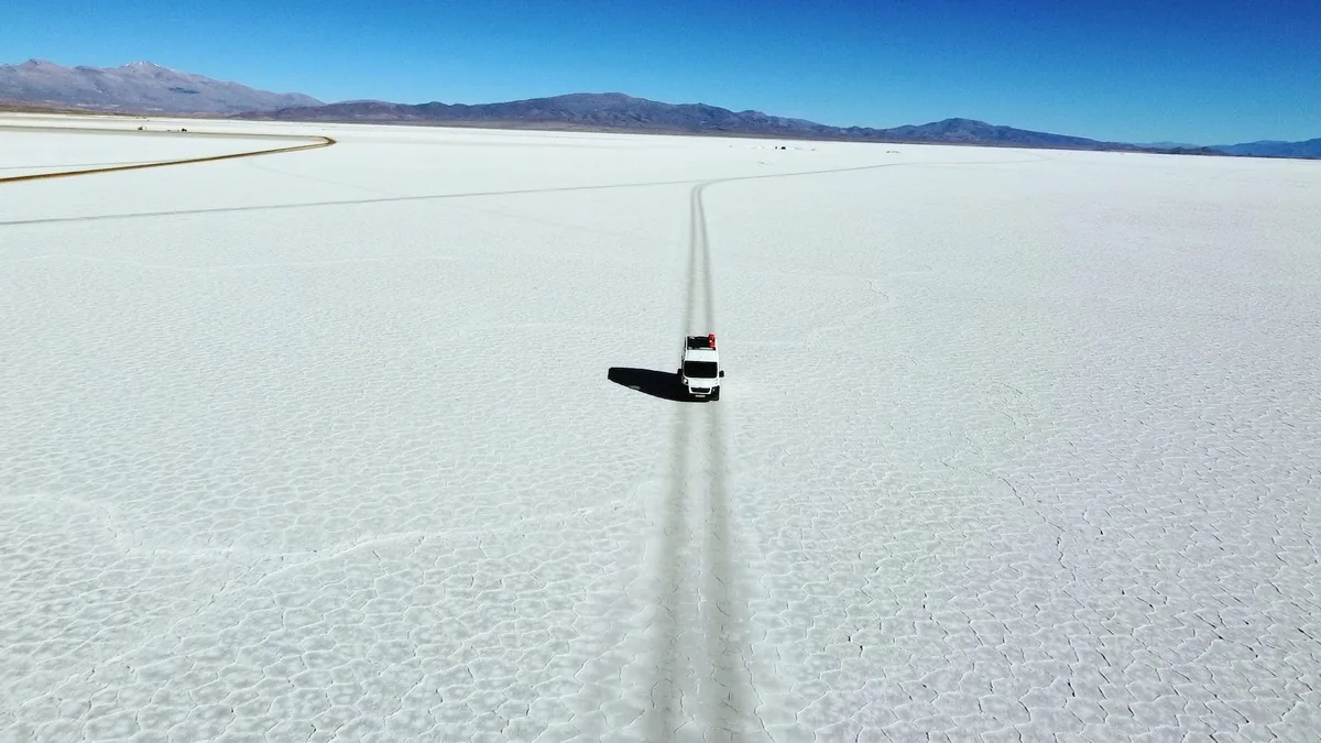 Overlander blanco con equipo de techo cruzando un gran salar agrietado. Viaje en van por un desierto de sal con montañas