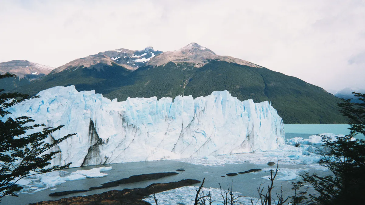 Gran pared de hielo del glaciar Perito Moreno en Patagonia con témpanos flotando en el lago y montañas boscosas
