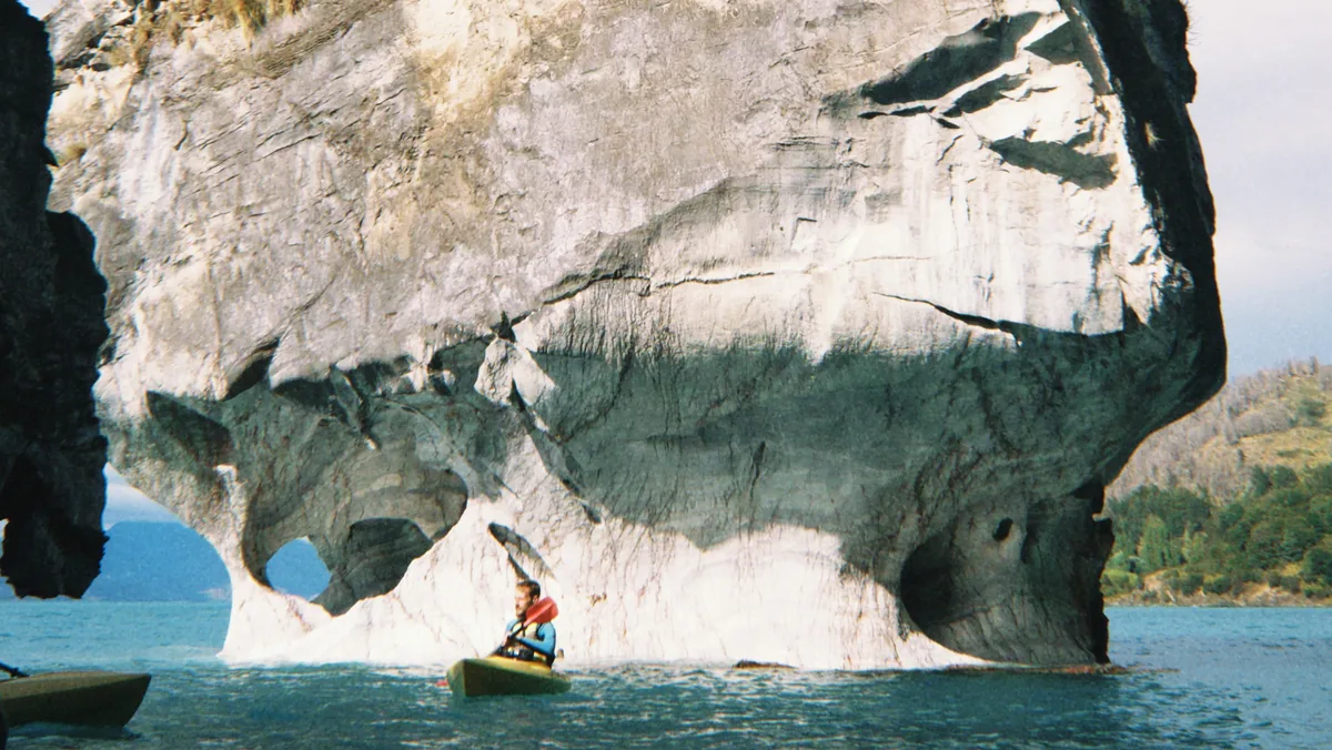 Persona en kayak amarillo frente a las impresionantes formaciones de mármol del Lago General Carrera, Patagonia chilena