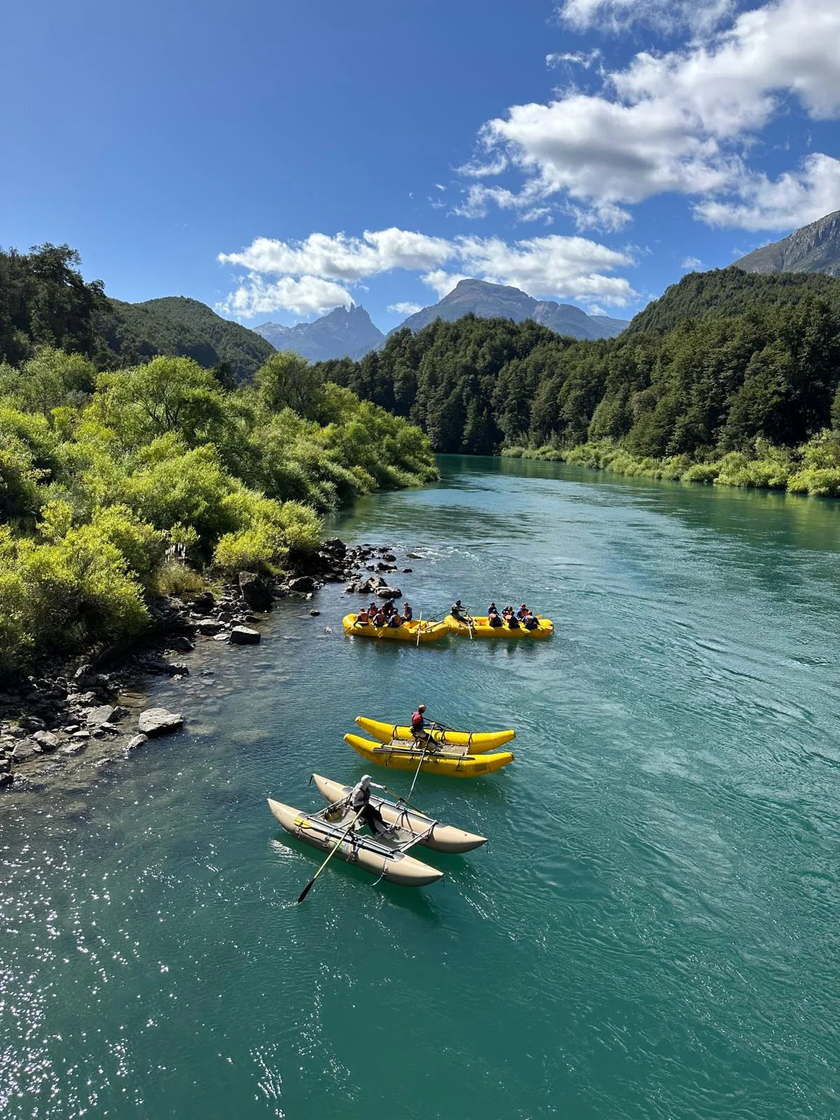 Aventureros remando en balsas y catamarán por un río turquesa, entre frondosos bosques y montañas imponentes
