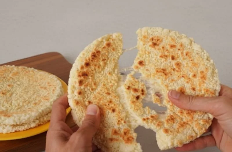 Dos manos estirando una arepa caliente con queso derretido, un desayuno rápido y delicioso para rutas overland