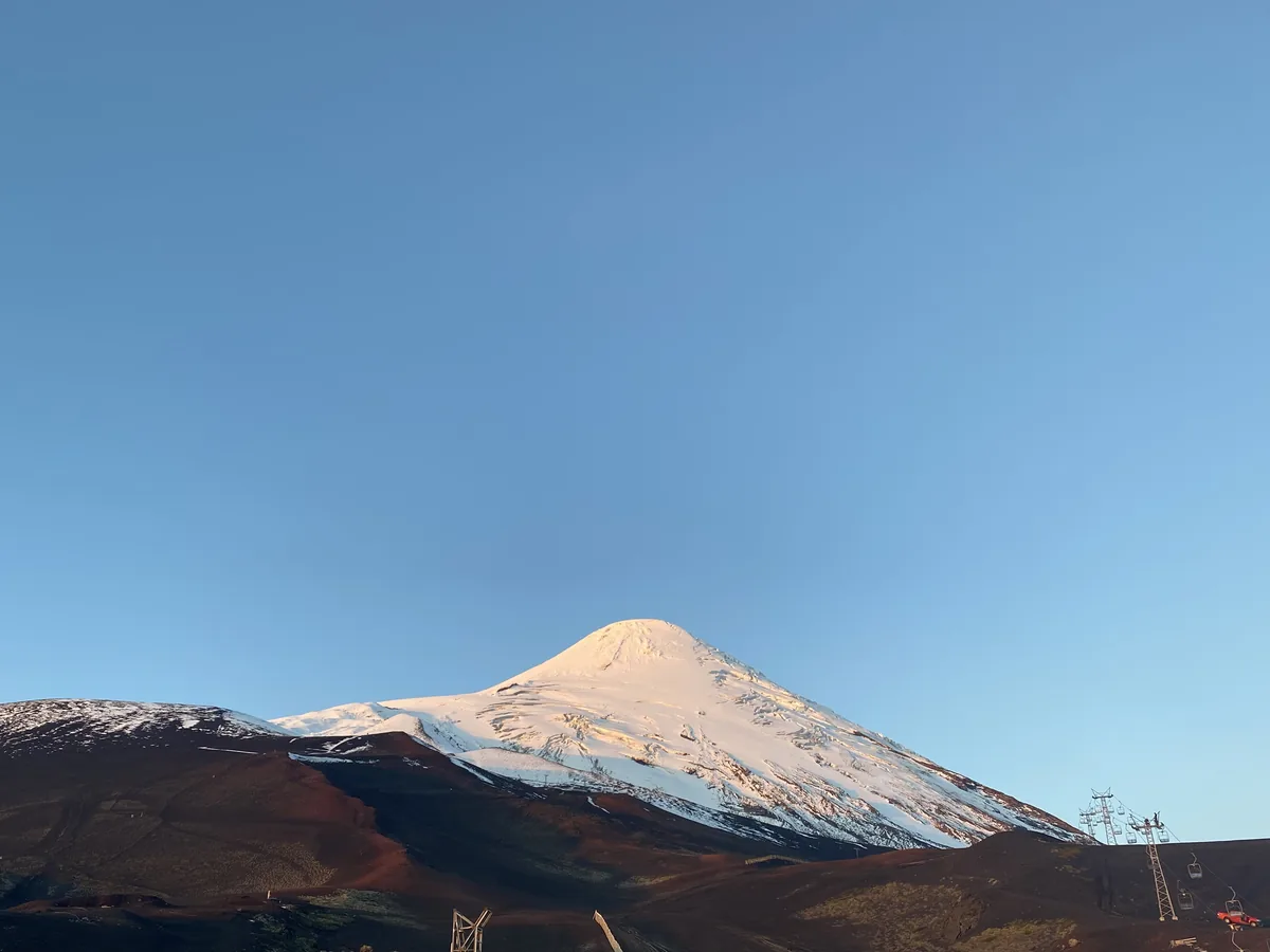 Volcán Osorno cubierto de nieve con terreno volcánico oscuro y telesillas de esquí en Chile al amanecer