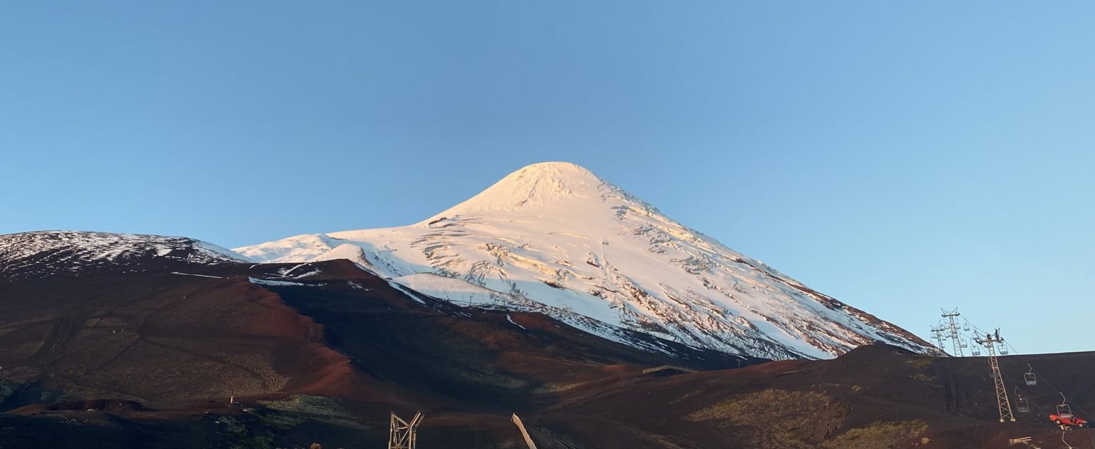 Volcán Osorno cubierto de nieve con terreno volcánico oscuro y telesillas de esquí en Chile al amanecer