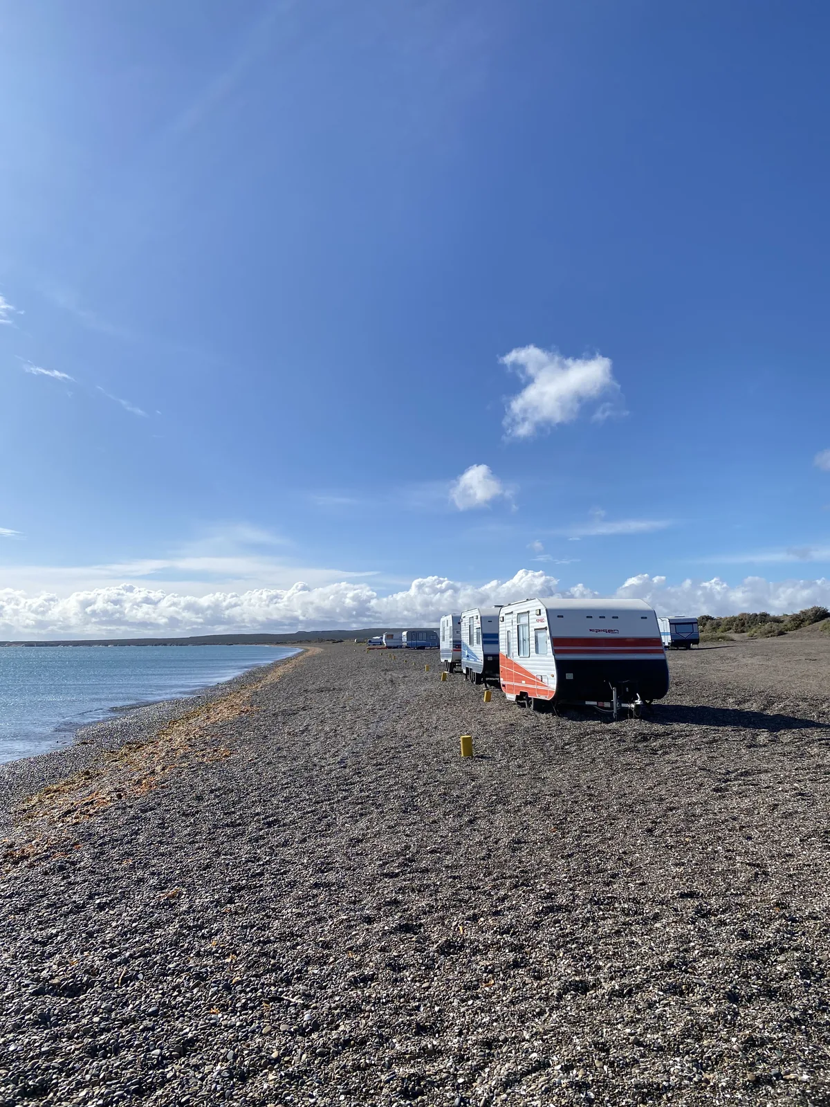 Caravanas rojas y blancas en una playa de guijarros junto al mar, listas para la aventura overland costera
