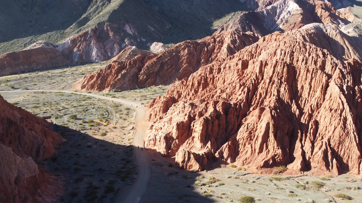 Vista aérea de un camino de tierra serpenteante entre montañas rojizas erosionadas, paisaje árido perfecto para overland