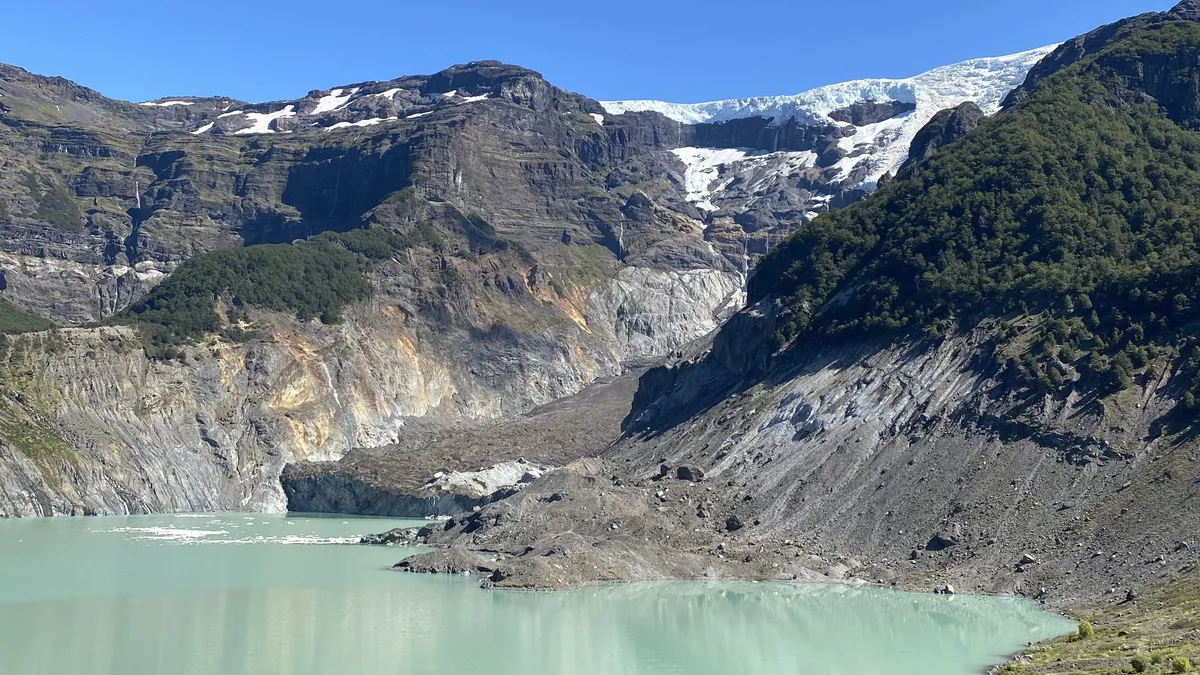 Glaciar andino imponente sobre un lago de aguas lechosas color verde azulado y laderas cubiertas de bosque
