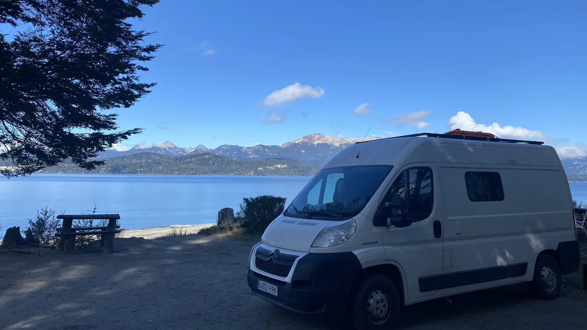 Camper van Citroën Jumper blanca estacionada junto a un lago azul en la Patagonia argentina, con montañas nevadas y una mesa
