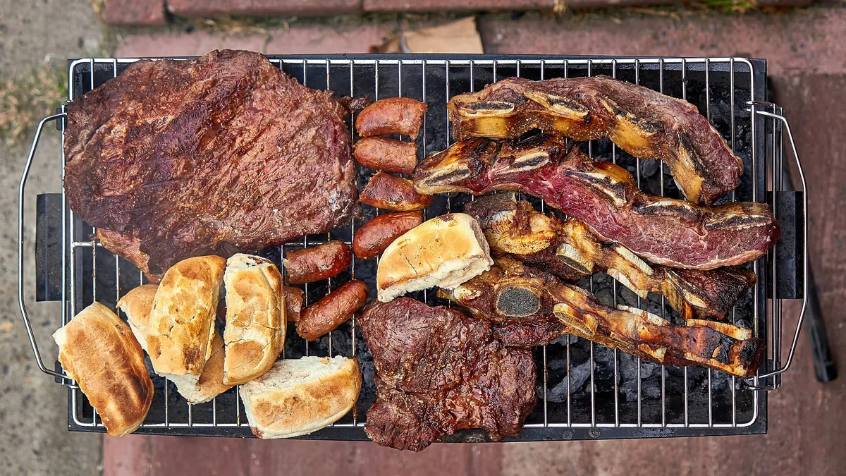 Asado argentino con tira de asado, vacío, chorizos y pan tostado en una parrilla portátil de viaje