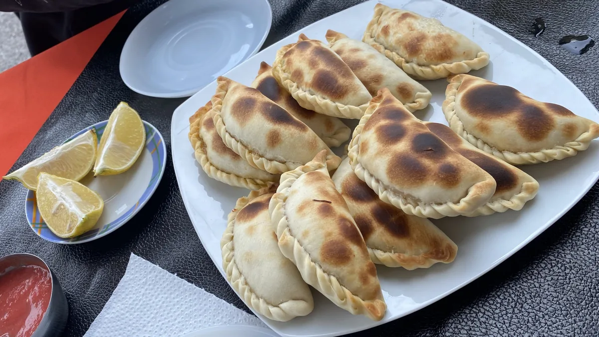 Plato de empanadas horneadas con bordes repulgados, acompañadas de gajos de limón y un cuenco de salsa roja