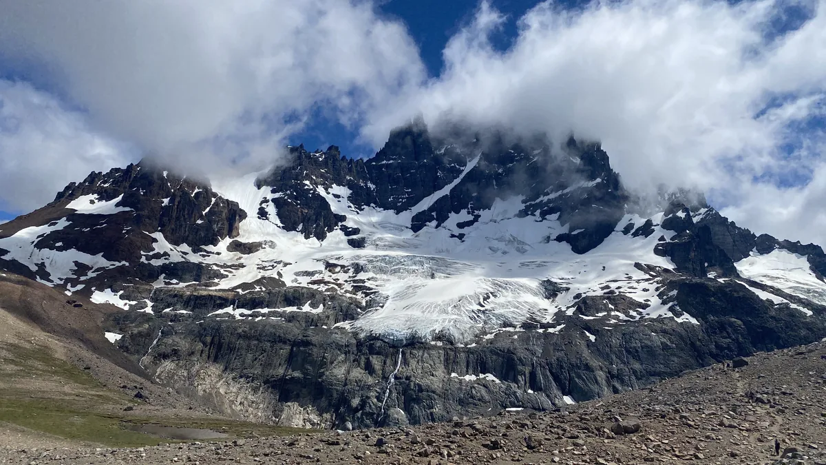 Glaciar majestuoso desciende entre picos rocosos y nevados, con nubes abrazando las cumbres de la Patagonia