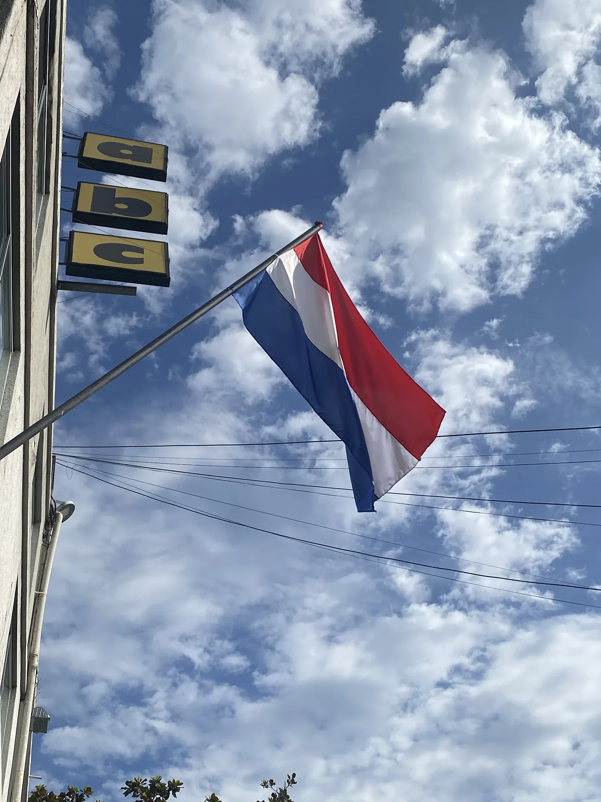 Cielo azul con nubes blancas sobre un edificio con letreros 'abc' y la bandera de Paraguay ondeando al viento