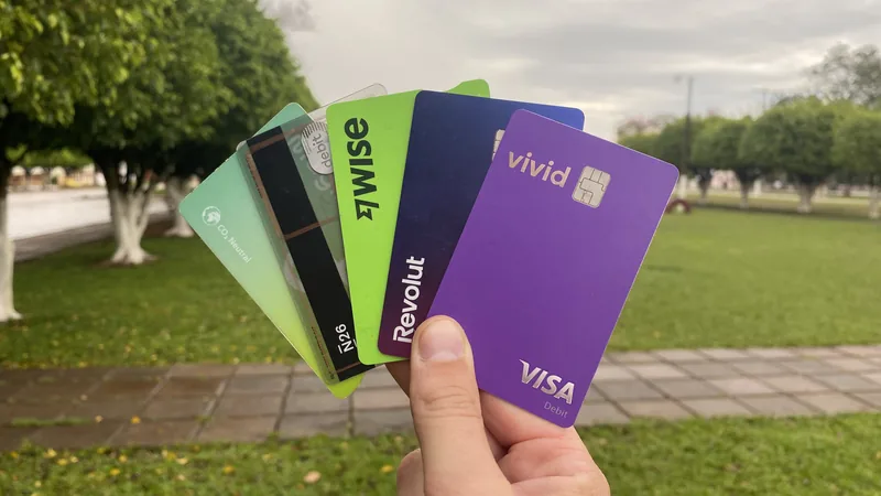 Mano mostrando tarjetas internacionales Wise, Revolut, N26, Vivid en un parque. Esenciales para gestionar finanzas en viajes