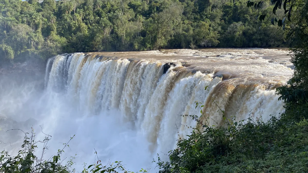 Cascada en Paraguay con fuerte caudal de agua marrón, rodeadas de densa selva tropical y bruma en la base