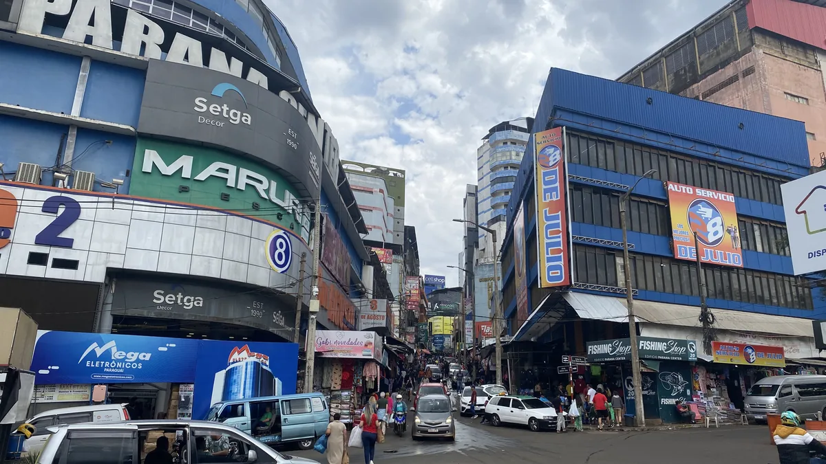 Ciudad del Este, Paraguay: calle comercial con tiendas, tráfico de furgonetas y peatones, bajo un cielo nublado